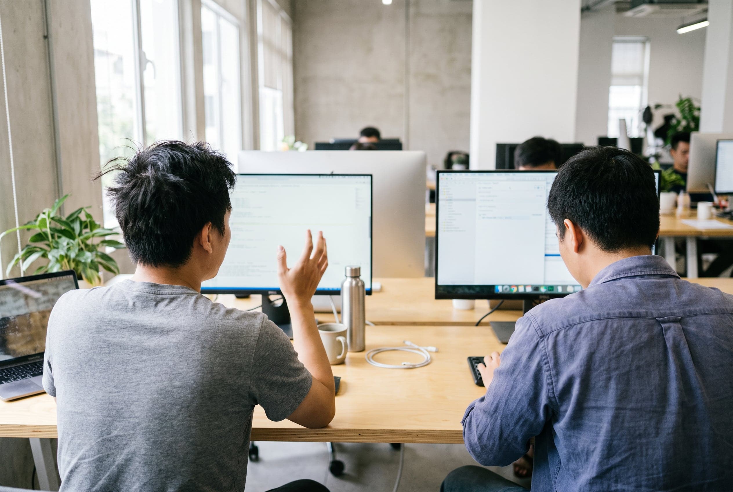 Hai lập trình viên xem sơ đồ kiến trúc hệ thống trên ba màn hình trong phòng làm việc tối